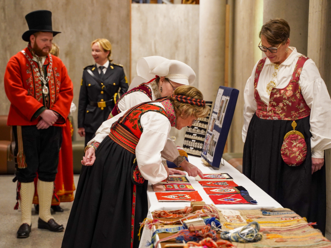 Dronning Sonja studerer produkt laga av kursdeltakarar på Tekstilsymposium 2024 saman med styreleiar Agnete Sivertsen i Norges Husflidslag. Kursdeltakarane har fått innføring i fire raudlisteteknikkar – metallknipling, perlebroderi, brillevev frå osebergfunnet og telemarksbinding. Dette er teknikkar som få kan, men som no blir formidla vidare. Foto: Liv Anette Luane, Det kongelege hoffet